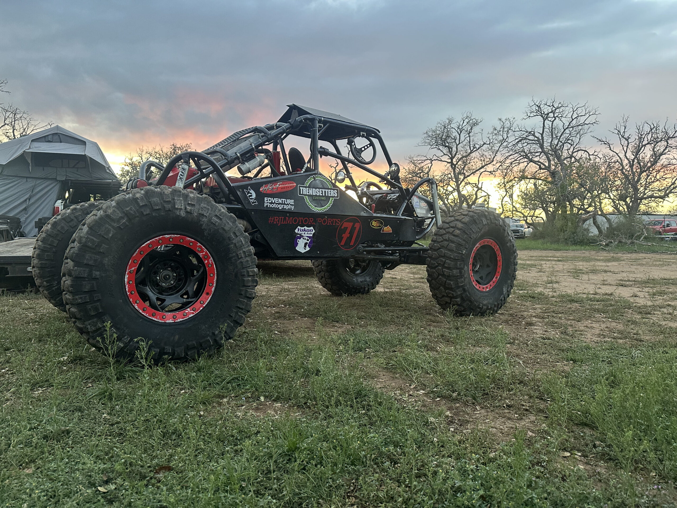 Off-road buggy with large tires and custom frame at sunset.