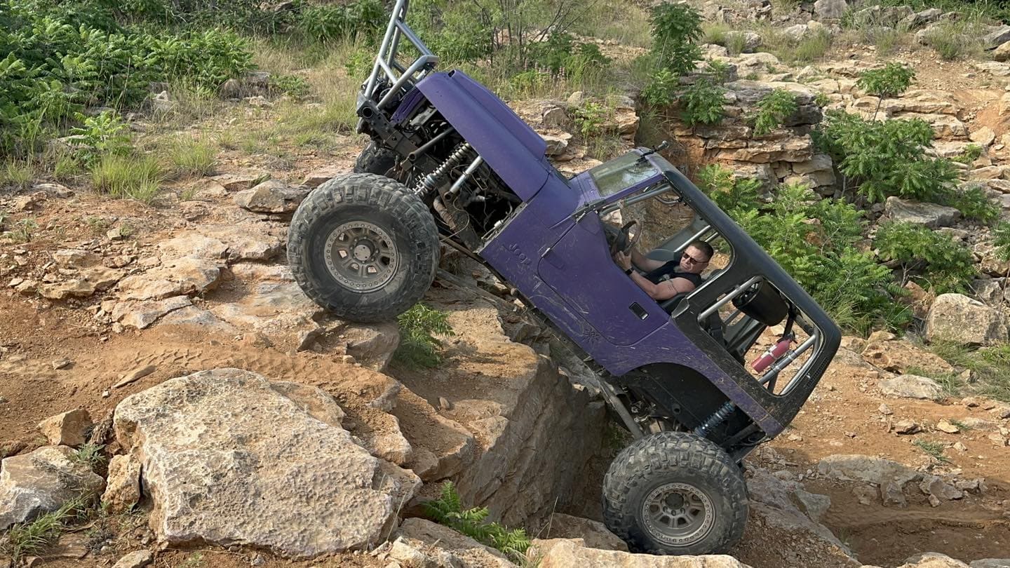 Custom purple off-road Jeep navigating rugged rocky trail.