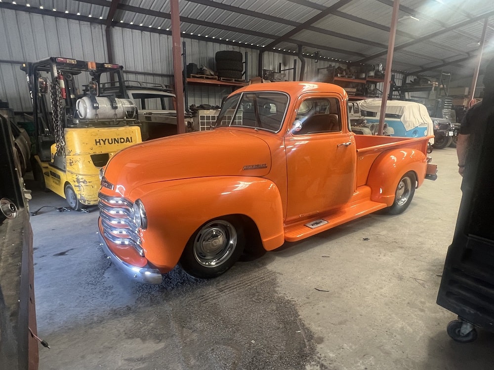 Classic orange vintage pickup truck in a workshop setting.
