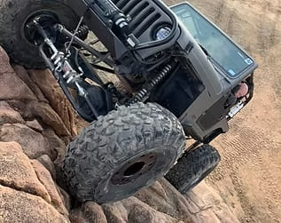 Custom off-road Jeep climbing rocky terrain with large tires.