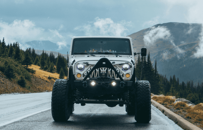 Custom Jeep with off-road modifications on scenic mountain road.