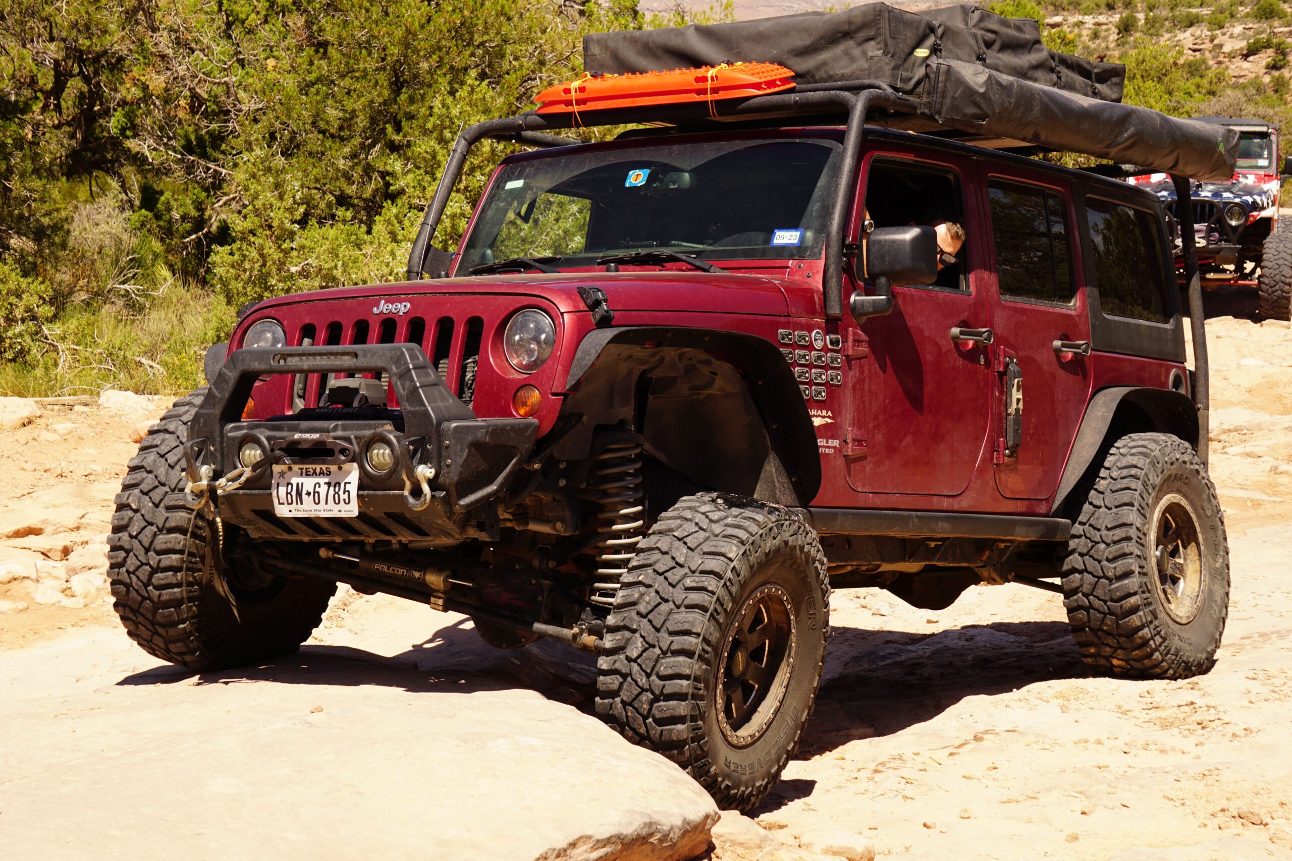 Red Jeep Wrangler with off-road tires and gear on a dirt trail.