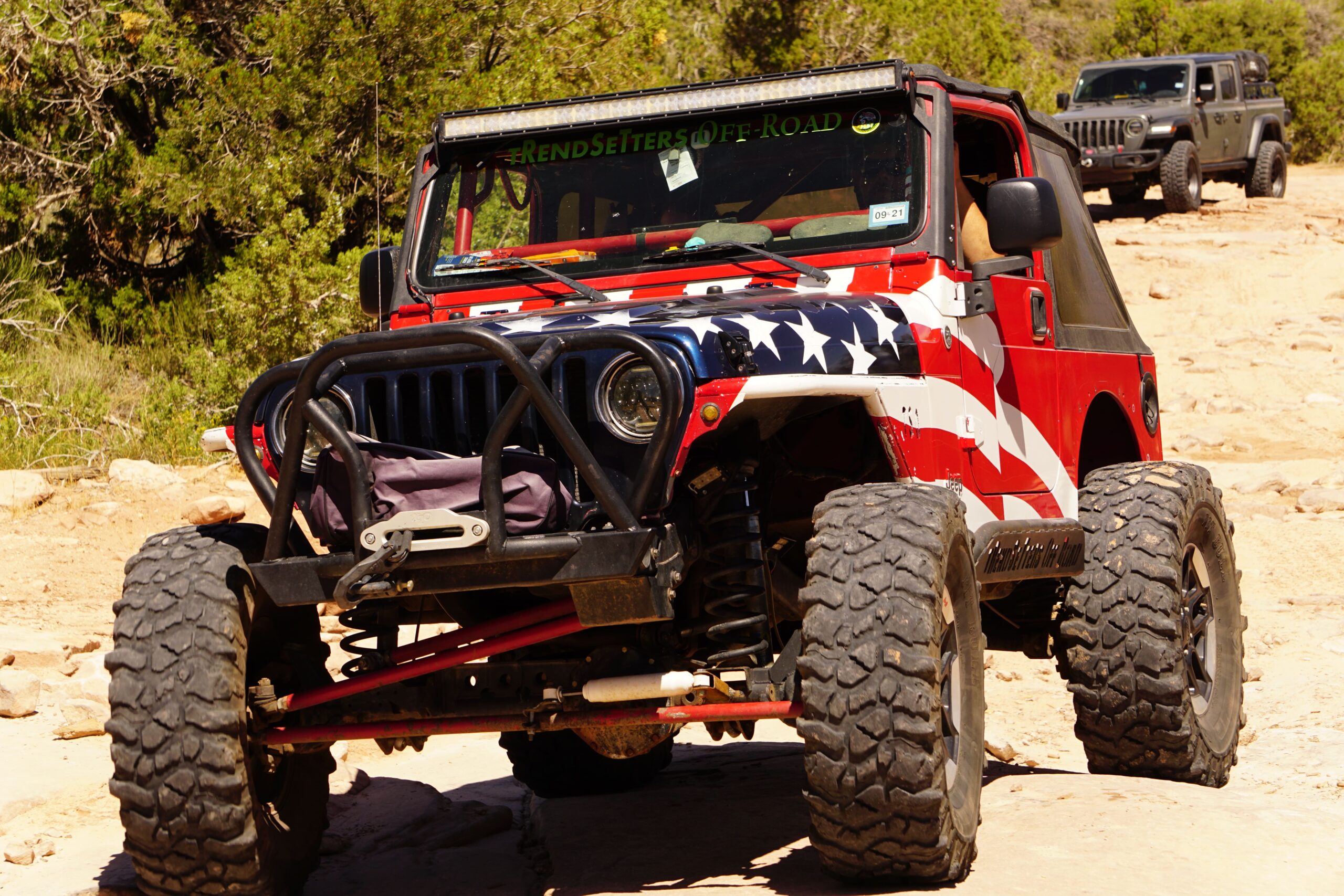 Custom off-road Jeep with patriotic American flag design and rugged tires.