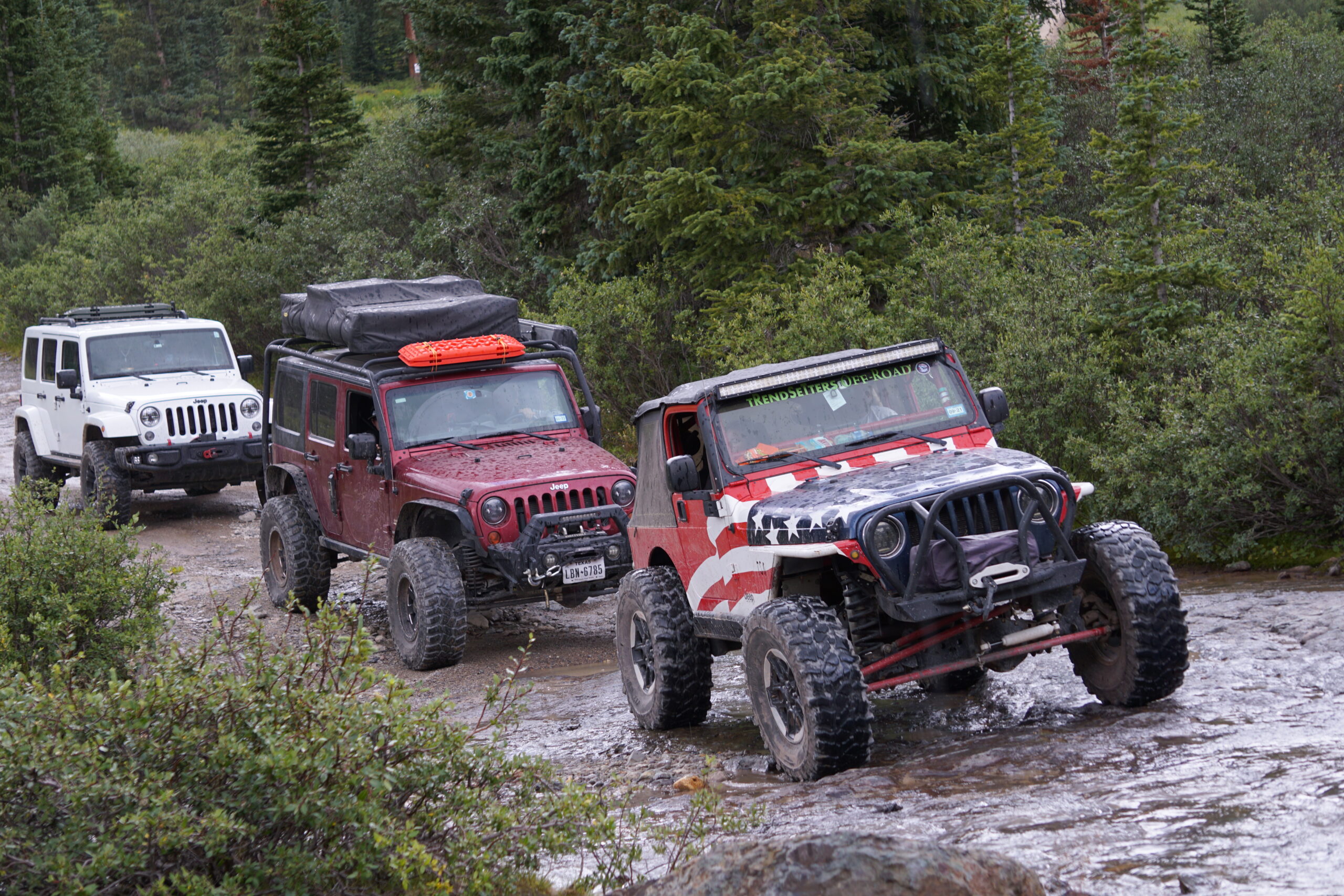 Off-road Jeep vehicles crossing a river in a forest setting.