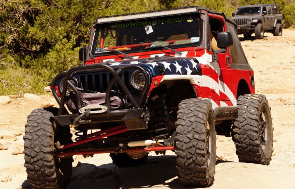 Off-road Jeep with custom American flag design and rugged tires.