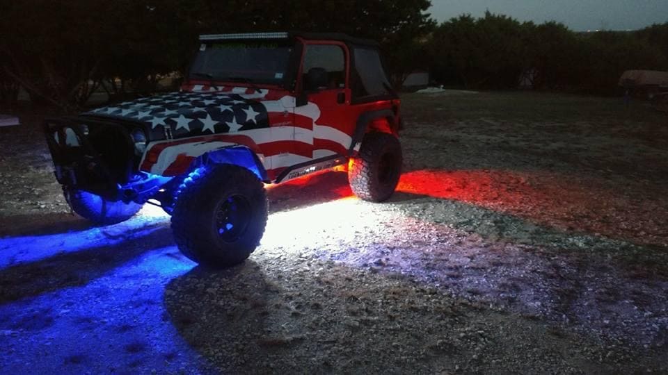 Custom Jeep decorated with American flag design and vibrant LED underglow lighting.