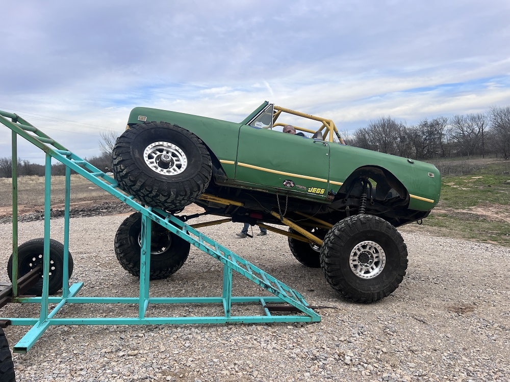 Custom-built green monster truck climbing an off-road ramp.
