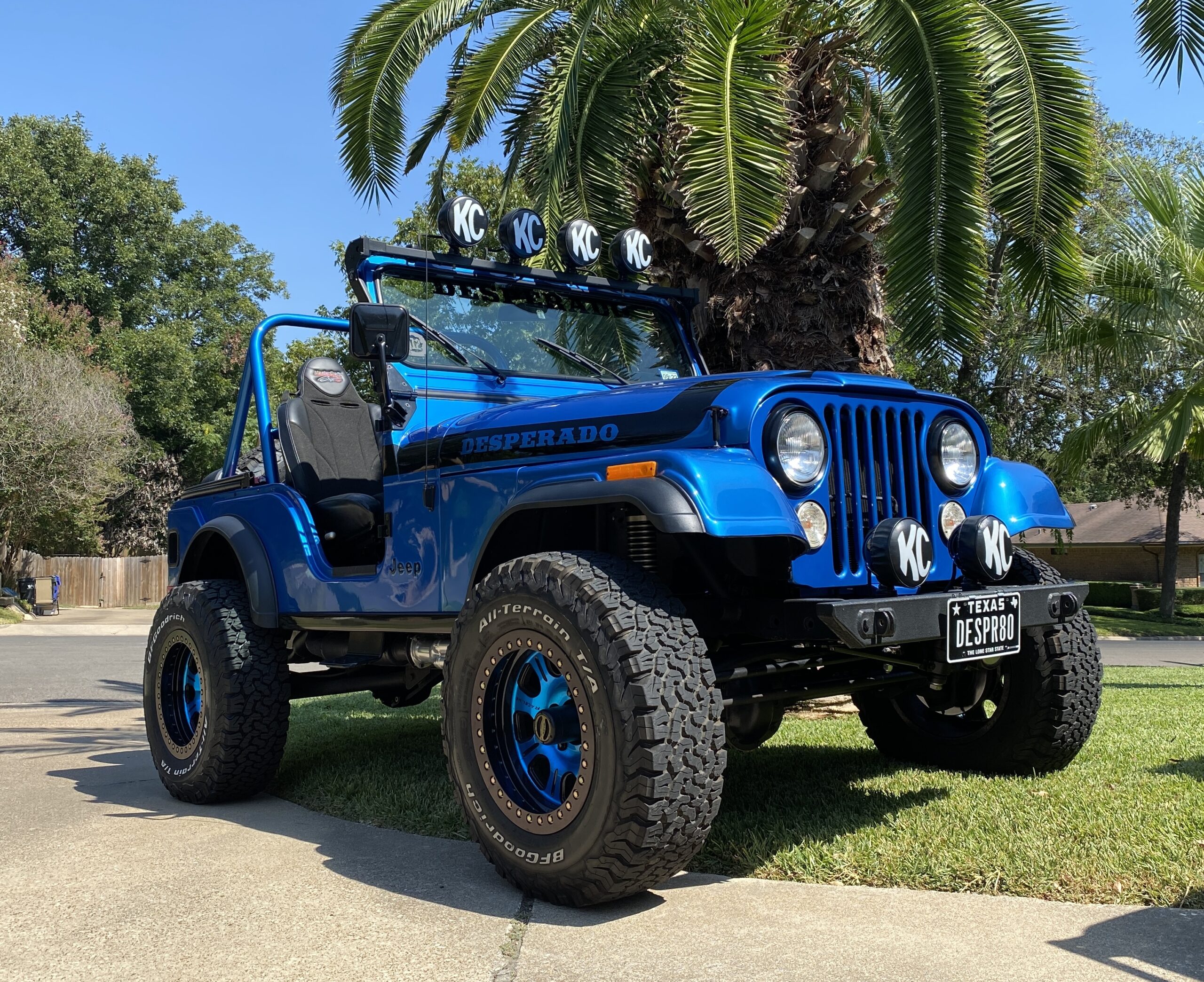 Blue Jeep Wrangler with off-road tires, KC lights, and custom modifications.