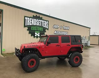 Custom red Jeep Wrangler with off-road tires and accessories at Trendsetters Customs.