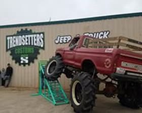 Monster truck with custom red paint and large tires at Trendsetters Customs.