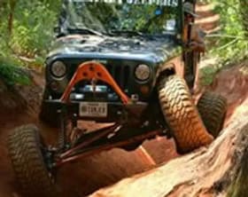 Off-road Jeep navigating rugged trail in forest terrain.