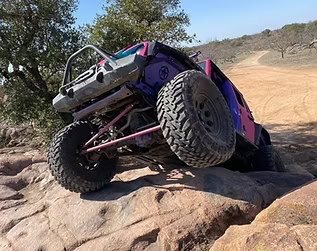 Custom off-road Jeep climbing rocky terrain with large tires.