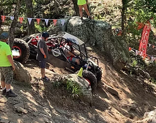 Off-road rock crawler vehicle navigating rugged terrain with team support.