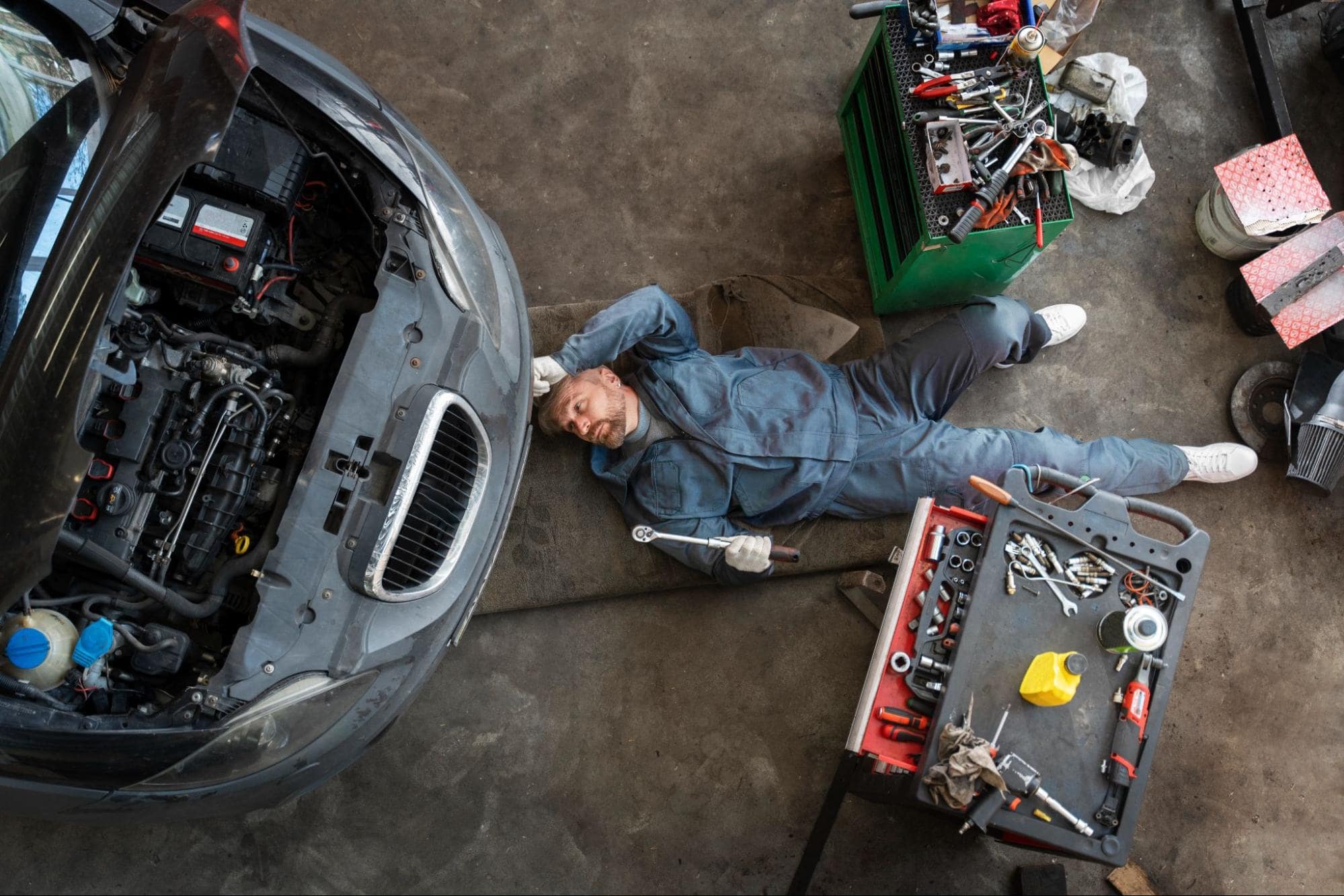 Auto mechanic inspecting engine under the hood of a car in a workshop.