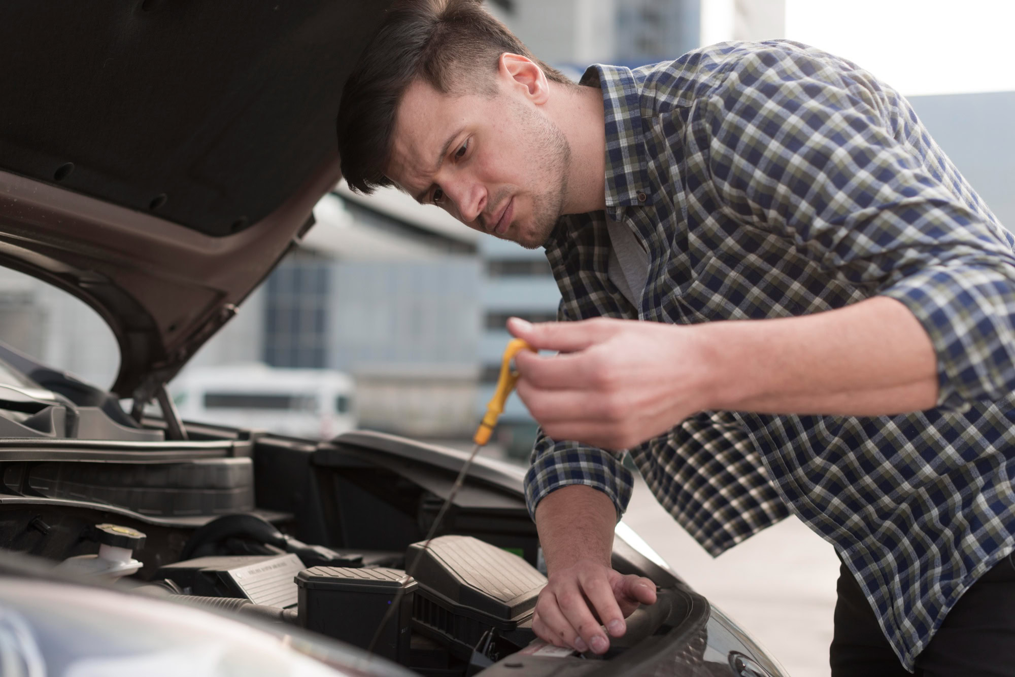 Man inspecting car engine for fuel injection maintenance in an urban setting.
