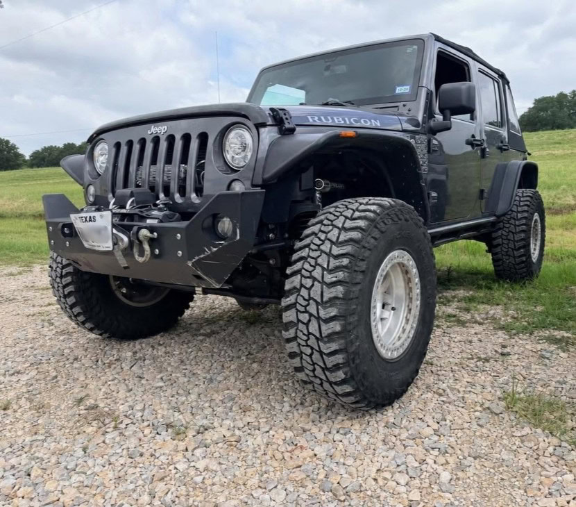 Black Jeep Rubicon with off-road tires and custom bumper in outdoor setting.