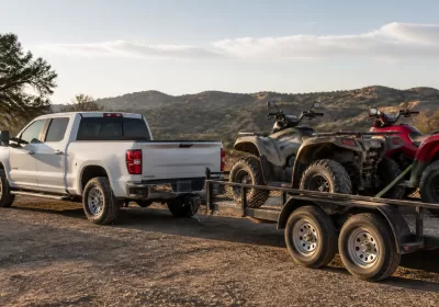 Custom off-road vehicles and ATVs on trailer at sunset.