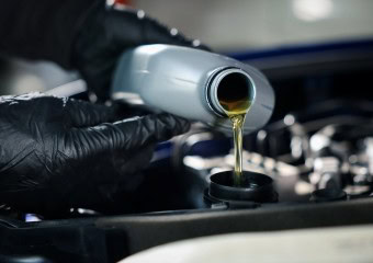 Technician pouring engine oil into a car engine during maintenance.