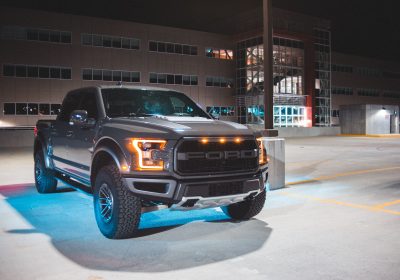 Black Ford Raptor truck parked in a well-lit parking lot at night.
