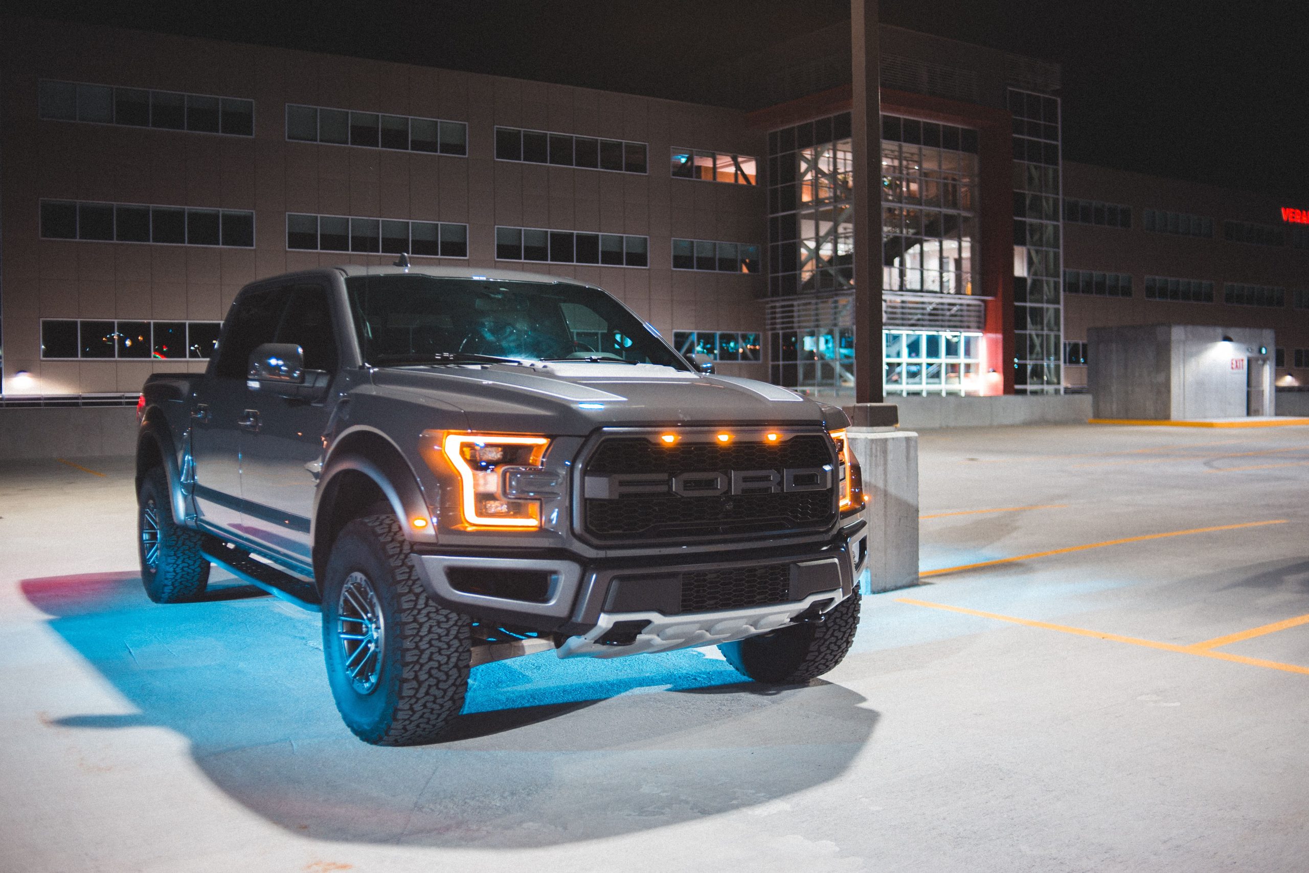 Black Ford Raptor truck parked in a well-lit parking lot at night.