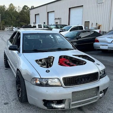 Modified Audi sedan with performance upgrades and custom hood in a workshop setting.