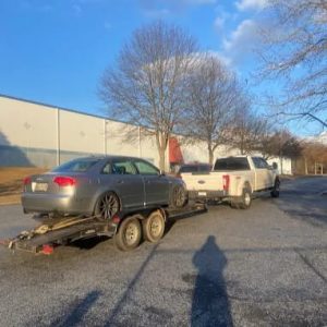 UAG Performance vehicle transport with a car on a trailer in a parking lot.