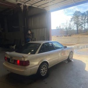 Vintage Audi convertible in a garage with open doors, outdoor scenery visible.
