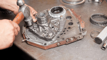 Technician working on a car transmission housing with tools on a workbench.
