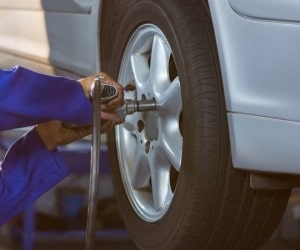 Technician repairing a car wheel with a pneumatic tool at Value Tires & Service.