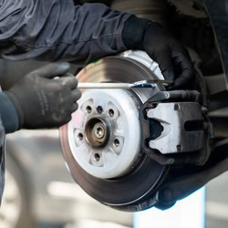 Technician replacing a car's brake rotor and caliper during brake service.