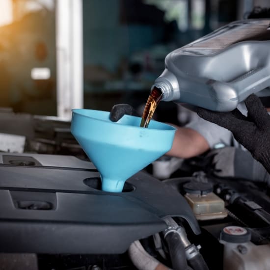 Mechanic pouring oil into car engine during oil change at auto repair shop.