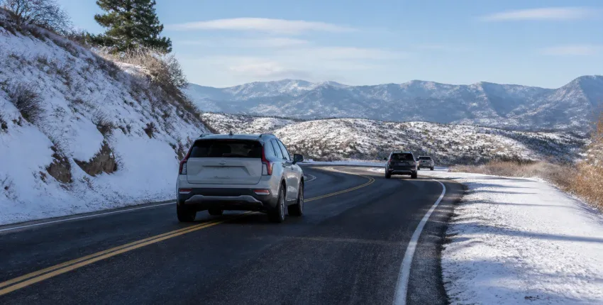 Vehicles driving on a mountain road with snow-covered landscape.