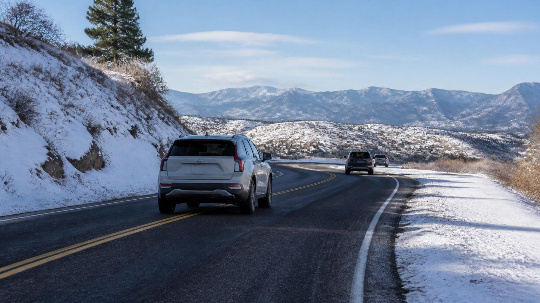 Vehicles driving on a mountain road with snow-covered landscape.