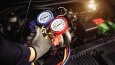 Technician checking car air conditioning system with gauges and tools.
