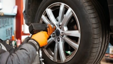 Technician inspecting car tire for wear and tear at auto service center.