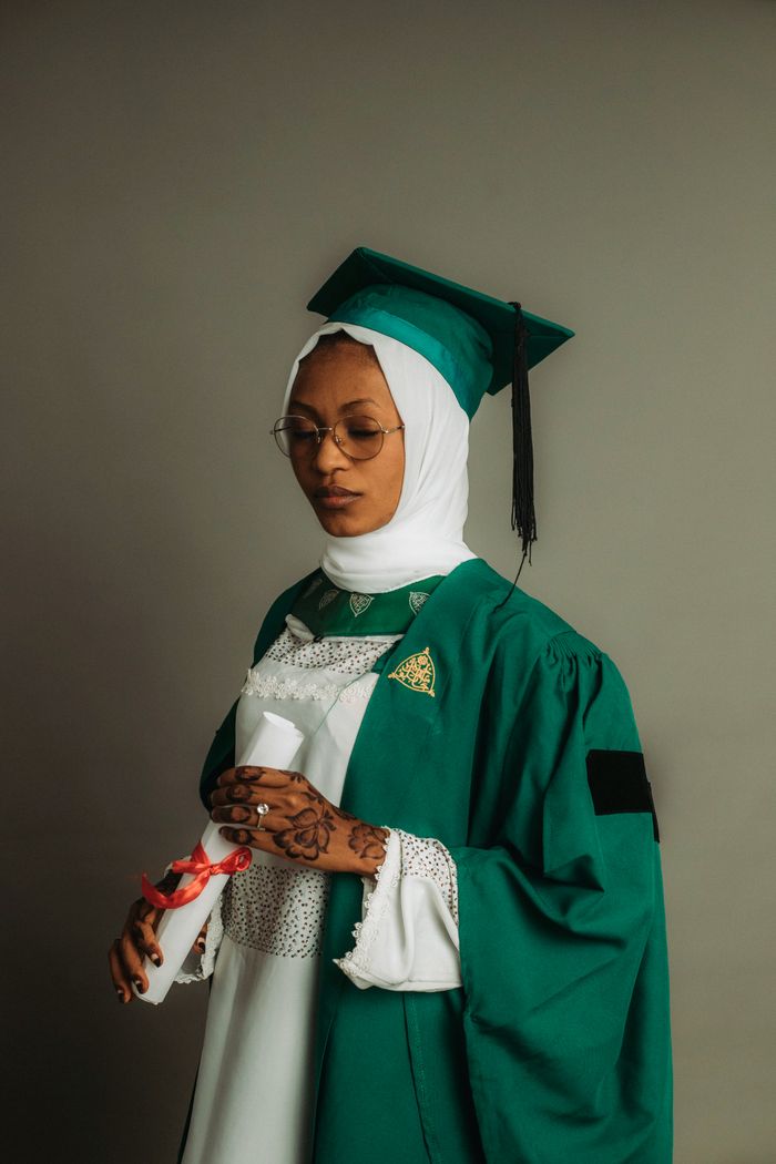 Young adult in graduation attire with henna, holding diploma in studio shot.