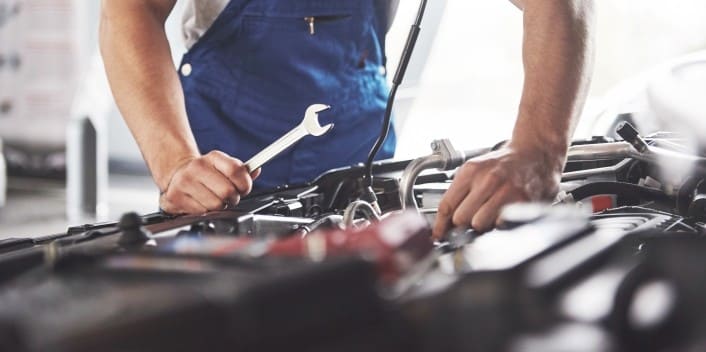 Auto repair technician inspecting car engine with wrench at Wallace Automotive. Expert vehicle maint.