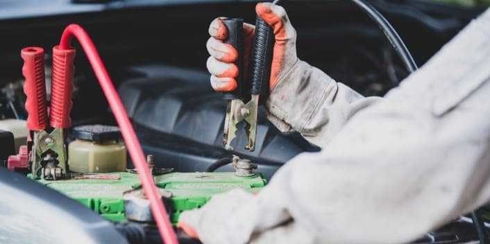 Technician testing car battery with multimeter for vehicle diagnostics.