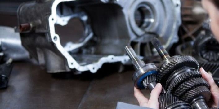 Close-up of a mechanic inspecting a car transmission gear assembly.