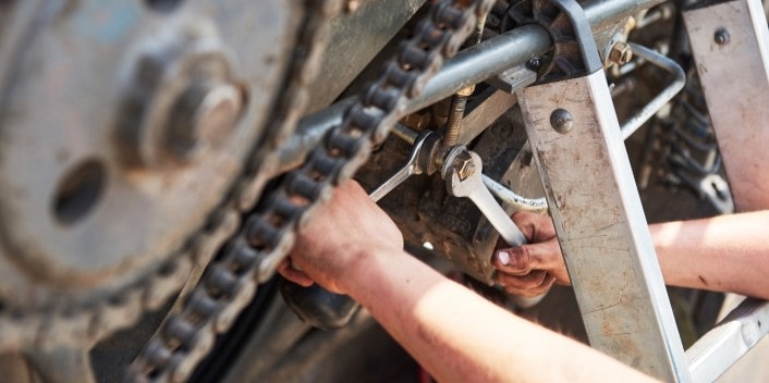 Engine repair technician working on motorcycle chain and sprocket.