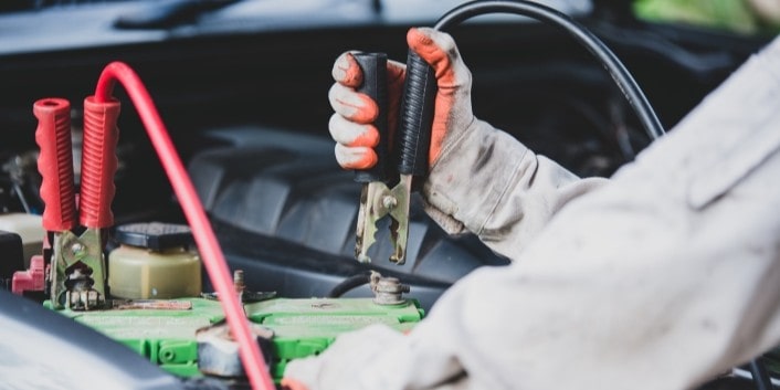 Technician testing car battery with multimeter in engine bay.