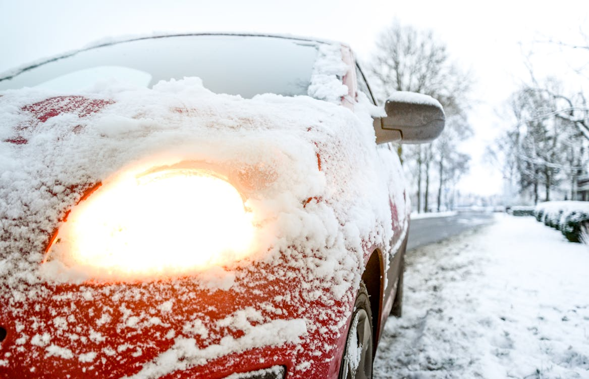 Winter snow-covered car with illuminated headlight in a snowy outdoor setting.