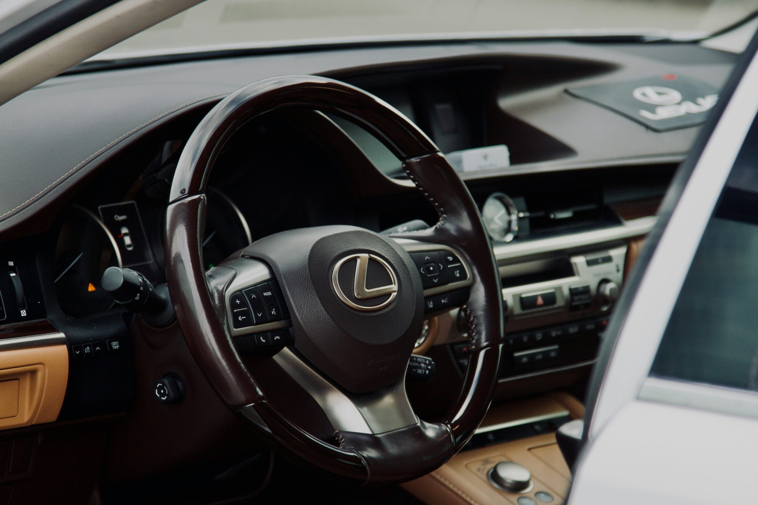 Close-up of Lexus car interior with steering wheel and dashboard controls.