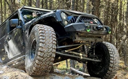 Offroad Jeep with large tires and lifted suspension on forest trail.
