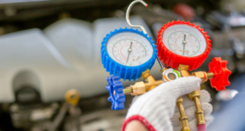 Technician holding HVAC manifold gauges for automotive air conditioning repair.