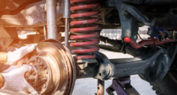 Mechanic inspecting vehicle suspension system with coil spring and shock absorber.