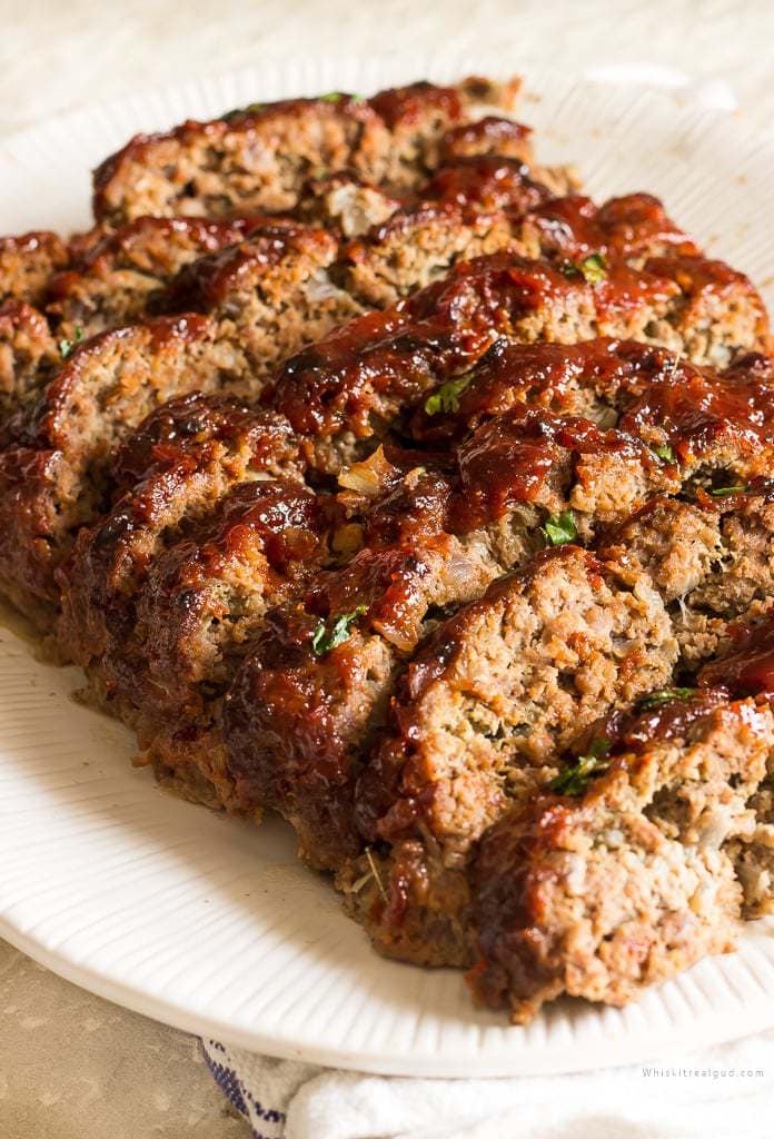  Slices of meatloaf with a brown sugar ketchup glaze on a serving plate. 
