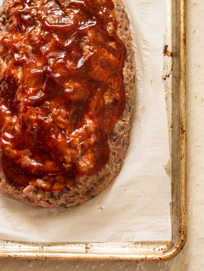 A raw meatloaf with brown sugar ketchup glaze on a parchment lined cookie sheet