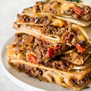 Sheet pan quesadillas that are stacked on top of one another with cheese, peppers and taco seasoning