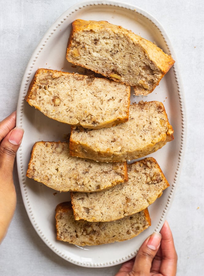 Plate of golden banana bread studded with walnuts on a serving dish